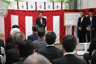 紅白の横断幕の前で市長が話をしている式典の様子の写真