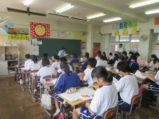 生徒が席に着いて、教科書を広げて本を読んでいる様子を左後方からクラス全体を写している授業中の写真