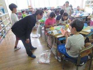 教室でグループに分かれて、折り紙で製作をしており、市長が手前のグループにの子ども達の製作の様子を興味深く見ている様子の写真