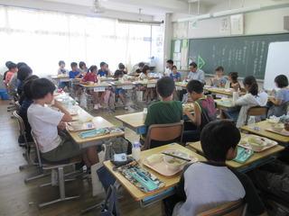 子ども達が教室の中で、向かい合って座っており、その中に市長も入ってみんなの顔を見ながら楽しい雰囲気で給食を食べている様子の写真