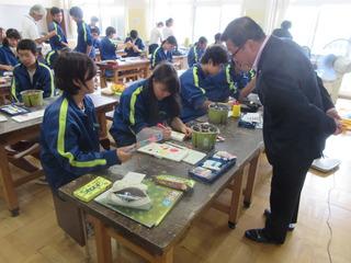 美術の授業中で生徒達が、マジックや絵の具を使って製作をしており、市長が女子生徒の作っている作品を見ている写真