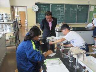 理科室にて、各テーブルごとに実験が行われており、防護用の眼鏡を着けた男子生徒と女子生徒が実験をしている様子を市長が覗き込んで見ている写真