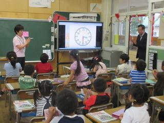 テレビに時計を表示して授業が行われており、女子児童の発表を市長と先生が手を叩いて賞賛している写真