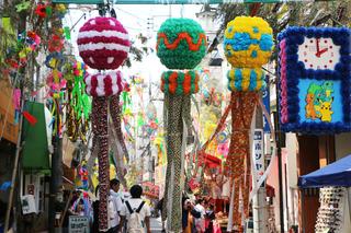 通りに沢山の七夕飾りが飾られていおり、通りに渡している棒に大きなくす玉のような飾りが3つ付けられ、その下を沢山のお客さんが歩いている写真