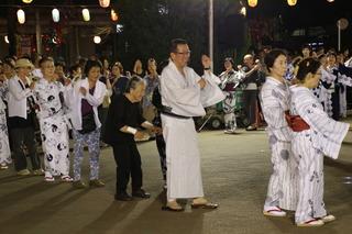 祭りで円になって沢山の参加者が踊りを踊っており、白い浴衣を着た市長が楽しそうに笑顔で踊りを踊っている写真