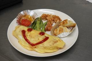 顔の描かれたオムライスと枝豆等の副菜が載せられている出来上がった料理がお皿に盛りつけられている写真