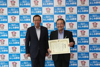毎日興業株式会社の関係者の男性が、賞状を手に持って笑顔で市長と一緒に写っている写真