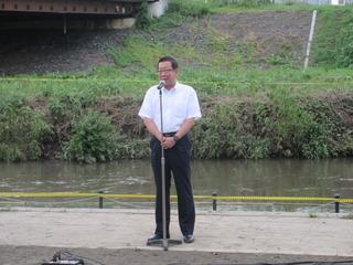 河川敷に置かれたスタンドマイクの前で市長が話をしている写真