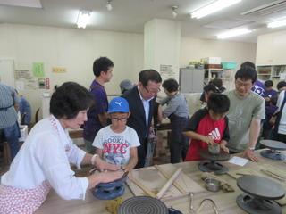 小学生の男子児童が陶芸の体験で、ろくろの上にねんどを置いて製作しており、その様子を市長が後ろから見ている写真