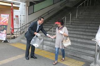 市長が駅の階段から降りてきた女性に、手渡しでキャンペーンのチラシを手渡ししている写真