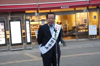 「ふじみ野市長」と書かれているタスキを肩にかけた市長が、街頭でスタンドマイクの前で話をしている写真