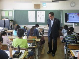 教室の授業中で児童達が習字をし、市長が子ども達の席の間を歩いて、書道の様子を見ている写真