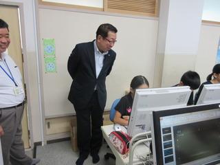 パソコン室での授業風景を見ており、子ども達がパソコンに向かって取り組む様子を後方から市長がみている写真