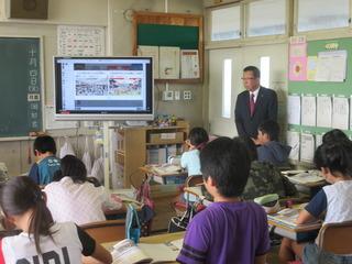 テレビに映像を映して授業が行われており、市長が教室の前の扉に立って、子ども達の授業のを見ている写真