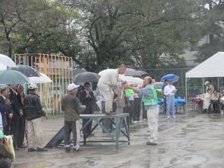 あいにくの雨の中表彰がおこなわれ、黄緑色のベストを着た男性が表彰を受けている写真