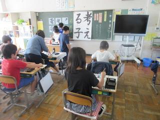 書道の授業が行われており、黒板には「考える子」と書かれた見本が貼られてあり、子ども達は自分の机で習字に取り組んでいる写真