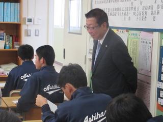 市長が生徒の机の横に立って、生徒の机の上の学習の取り組む様子を見ている写真