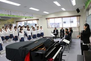 音楽室にて、市長や関係者の方々がパイプ椅子に座っており、その前で大井中学校音楽部の皆さんが合唱をしている写真