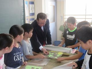 机の周りに児童が集まっており、子ども達が作った作品を市長が手に持って見ている写真