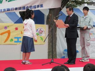 市長が舞台の上で、女子児童に表彰をしている写真