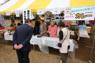 市長が出店を回っており、テントの下でお店を出している女性の出店者とお客さんに声をかけている写真