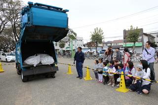 ゴミ収集車のトラックの後ろが開けられており、ゴミの入る荷台の様子を来場者の親子連れ方々が見ている写真