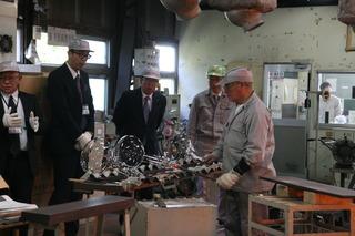工場内でガラス製品が作られており、市長と関係者の方々が視察をしている写真