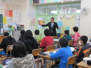 教室の右前方で、市長が席に着いている子ども達に両手を広げて話をしている写真