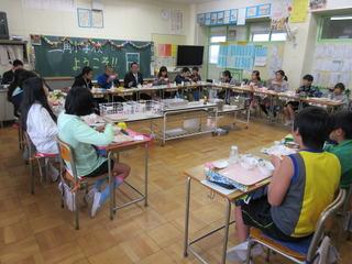 給食の時間で、机を中央に向けて並べて座っており、市長は黒板の前の子ども達の間に座って、楽しそうに給食を食べている写真