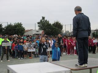 スポーツフェスティバルにて代表の2名の男子選手が、右手を挙げて選手宣誓をしており、その後ろには参加選手がチームのプラカードを持って整列している写真