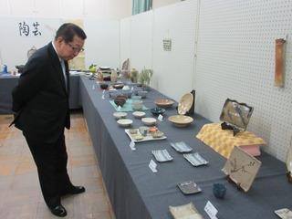 机の上に沢山の陶器の作品が展示されており、市長が作品をじっと見ている様子の写真