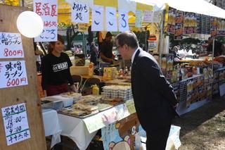 商品が沢山並べられており、「こころ」と書かれているのれんのお店の女性の店員さんに市長が声をかけている様子の写真