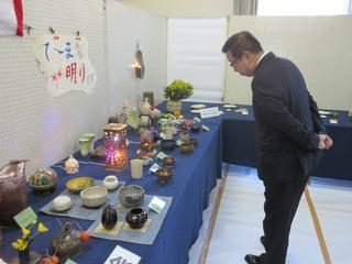 机の上に沢山の陶芸品が並べられており、市長が両手を後ろに組んで、じっくりと見ている様子の写真
