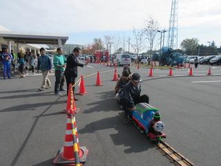 赤いポールで電車が走るコーナーが設置されており、キャラクターの電車に乗っている子どもに市長が手を振っている写真