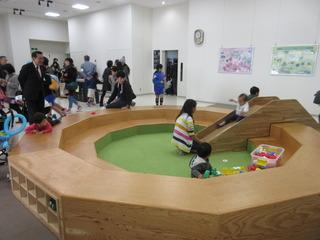 木製で小さな子どもが遊べるコーナが作られており、滑り台を滑っている子どもを市長が見ている写真
