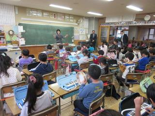 鍵盤ハーモニカを演奏しているクラスの授業風景を、市長が前方の入り口付近で見ている写真