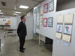 壁に展示されている書の作品を市長が手を後ろに組んでじっくりと見ている写真