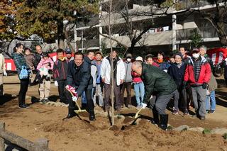 福岡中央公園桜の木植樹式で、市長と緑色のジャンパーを着た男性がスコップを持って植樹をしており、その後ろに植樹祭の参加者が集まって一緒に写っている写真