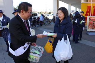 ふじみ野市長と書かれているタスキを肩にかけた市長が街頭に立ち、買い物袋を手にかけている女性にキャンペーンのチラシを手渡ししている写真