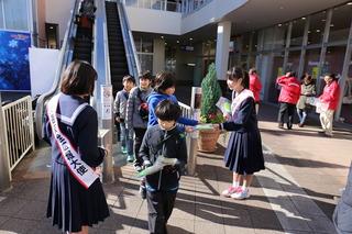 花の木中学校の五十嵐 梢さん達が、街頭のエスカレーターから降りてくる子供たちに、キャンペーンのチラシを手渡ししている写真