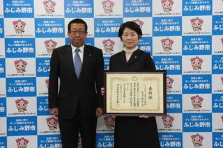 大津 朋子校長が額縁に入った表彰状を手に持って、市長と一緒に写っている写真