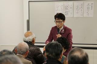 講演会でホワイトボードの前で講演する佐藤 良子さんの話を聞いている参加者の写真