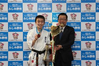 空手着にメダルを下げた葦原中学校の増野 宏希さんと増野さんの優勝トロフィーを持った市長が記念撮影している写真