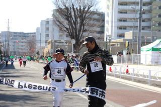 野球のユニフォームを着た男の子と大人の男性が一緒にゴールテープを切っている写真