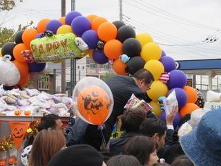 風船で作られたゲートの前で市民にお菓子を配っている市長の写真