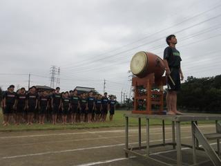 生徒達が整列し前方の壇上に太鼓とバチを持った生徒が立っている写真