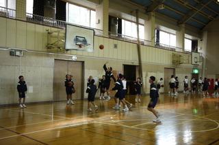 体育館で体育の授業が行われており、バスケットボールの試合の中で、ゴール下の一人の生徒がシュートをしている写真