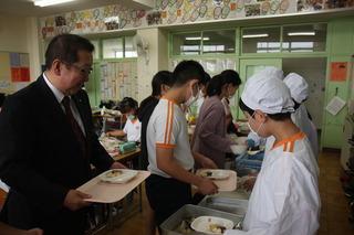 給食の配膳をしている子供たちと並んで受け取っている市長の写真