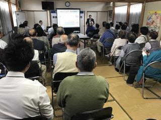 和室の集会場にたくさんの高齢者が集まって話を聞いている写真