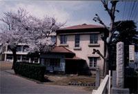 玄関横に桜の木が生えている木造モルタル2階建ての西洋風建築である旧大井村役場の写真